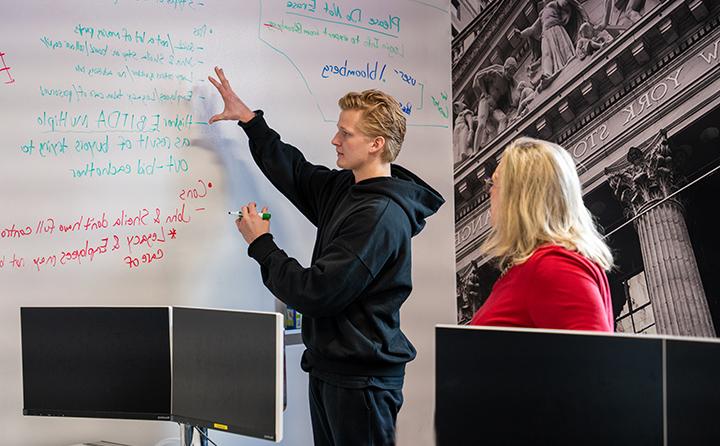 戴恩·麦克纳尔蒂24岁(右), talks through a finance project with Carmel Boyer 商学院 dean Dr. Susan Kuznik (left) in BW’s Bloomberg Business Research Center.